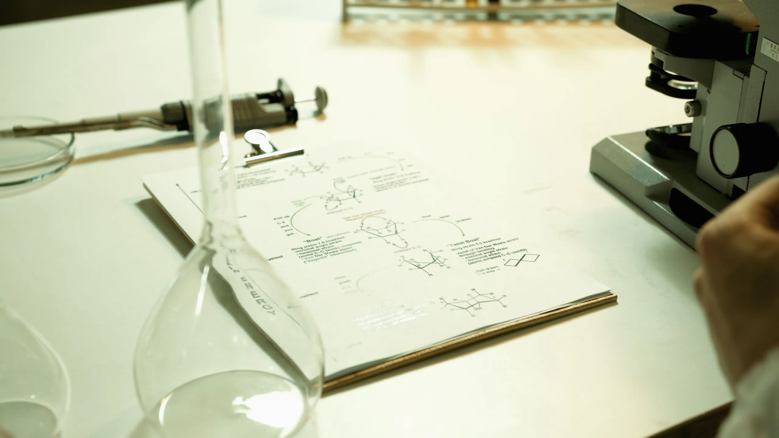Open notebook with biochemistry diagrams on a white bench, beside a flask and a microscope.